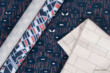 Three rolls of Marvel-themed fabric laid diagonally on a Spider-Man navy blue wallpaper. The fabrics show different patterns: a light gray spiderweb design, a navy and red geometric design, and an off-white brick pattern.