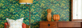 A styled interior scene showing a wall covered in green Spider-Man patterned wallpaper, with part of a wooden cabinet, a floor lamp, decorative vases, and a window visible.