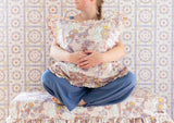 A girl with blond hair holds a Disney Rapunzel pillow in her arms as she sits on top of a Rapunzel stool in front of Rapunzel medallion wallpaper
