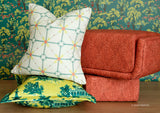 Three decorative throw pillows arranged on a wooden surface against a green Spider-Man patterned wallpaper background. The top pillow is off-white with a teal geometric lattice pattern and small yellow and orange accents.