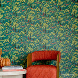 A styled interior scene featuring a red upholstered armchair in front of a wall covered in green and yellow Spider-Man patterned wallpaper. A small white side table with books and a pumpkin sits on the left.